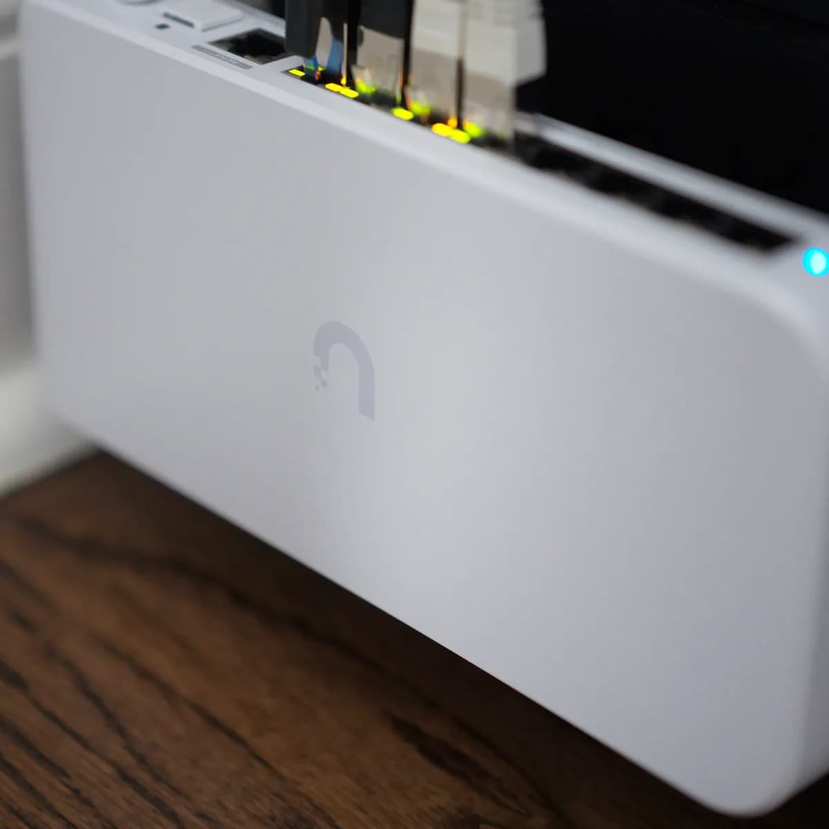 A USW Flex 2.5G 8 PoE standing on a hardwood floor against a baseboard, five ports patched and lit, status LED blue.