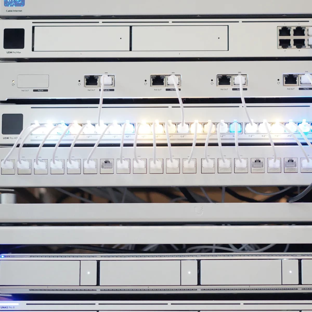 A lit UniFi switch over a fully patched 24-port panel, white cable looped to every port.